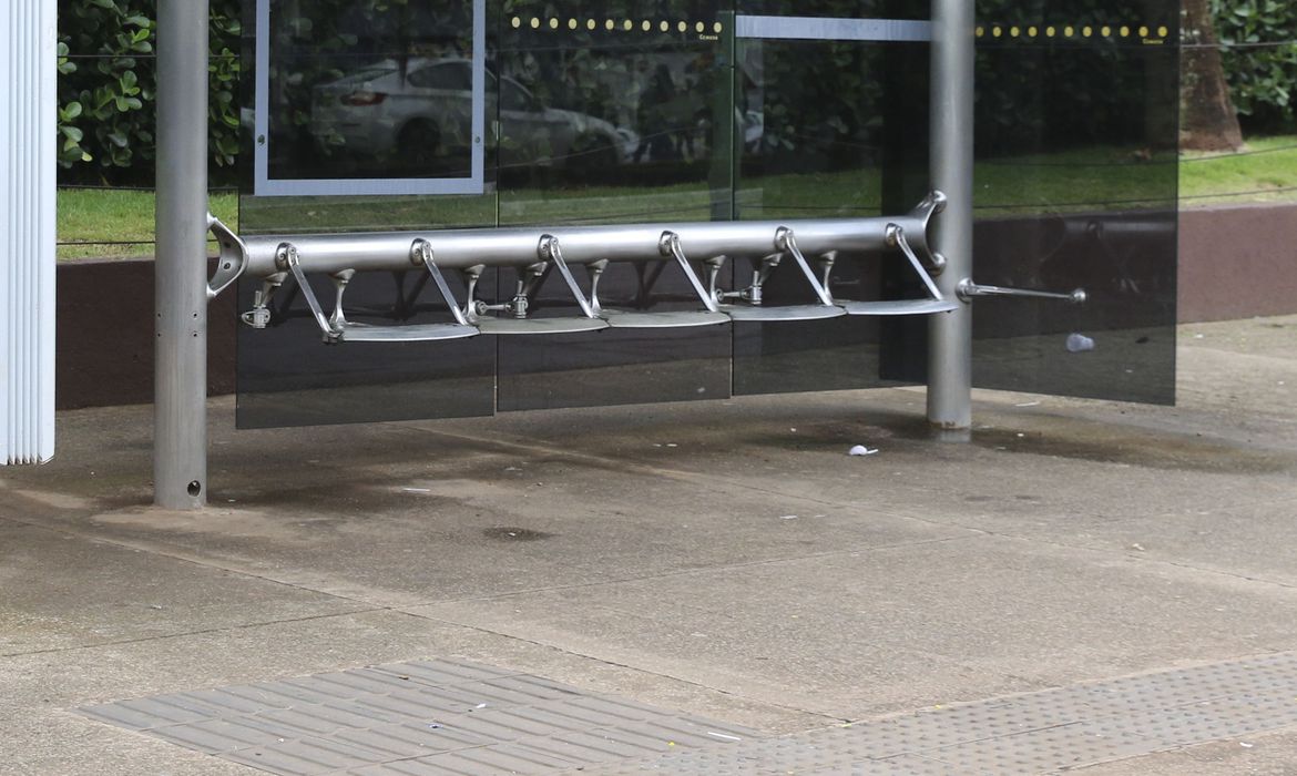 Parada de ônibus de vidro com bancos com arquitetura hostil